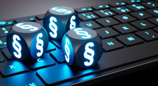 Datenschutz - schwarze Würfel mit blau leuchtendem Paragraphen Symbol liegen auf einer schwarzen Computertastatur mit ebenfalls blau leuchtenden Buchstaben