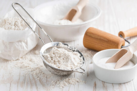 Various ingredients for baking on a white wooden table, including baking powder or baking soda.