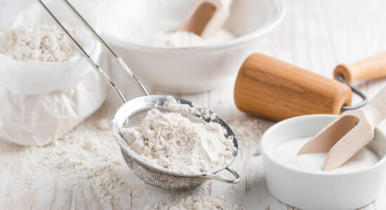 Various ingredients for baking on a white wooden table, including baking powder or baking soda.