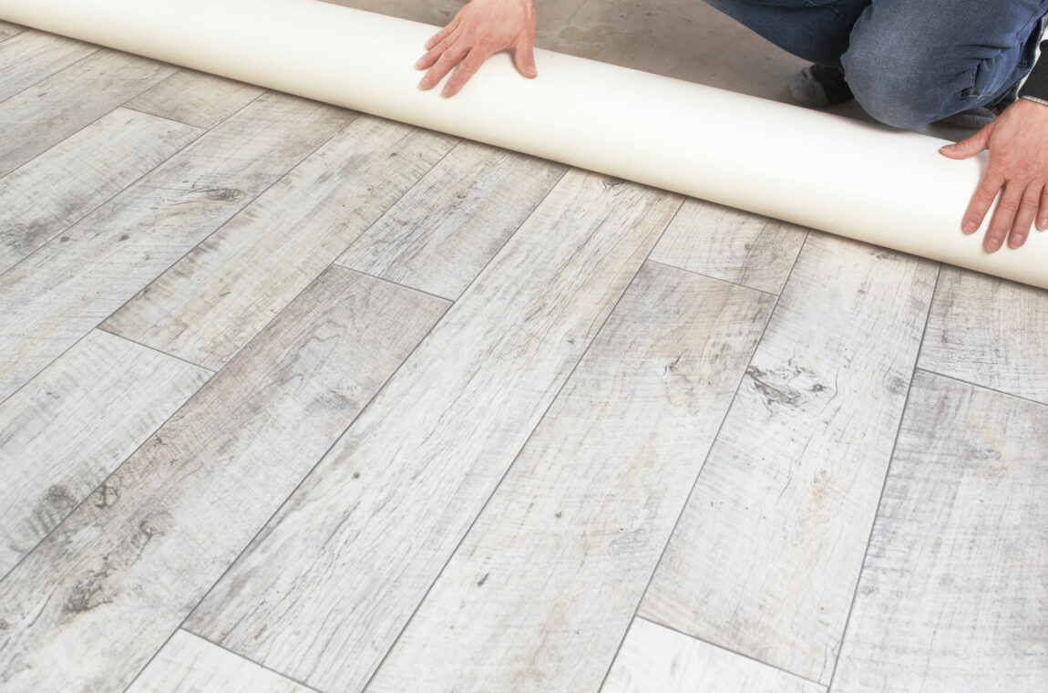 A PVC floor covering in a gray-white wood look is rolled out