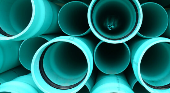 Mint-colored PVC pipes (polyvinyl chloride) stacked from the front so that you can look inside the pipes.