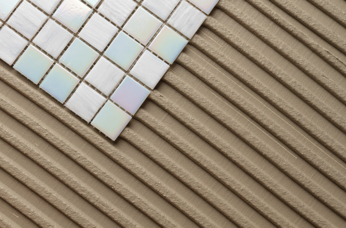 A floor is being tiled in the bathroom, you can see mosaic tiles and tile adhesive