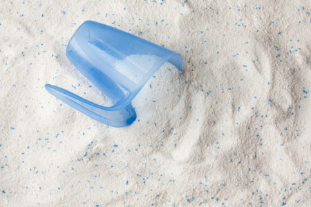 Detergent or washing powder. White powder with some blue particles. There is a dosing container on top