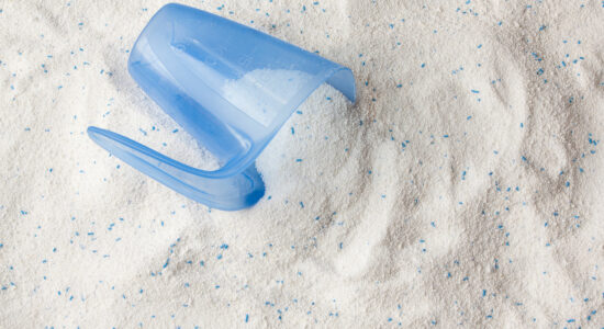 Detergent or washing powder. White powder with some blue particles. There is a dosing container on top